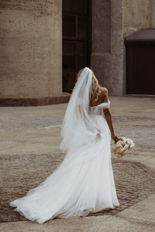 Romantic bridal dress featuring shimmering layers of tulle, intricate corset detailing, and elegant off-shoulder sleeves, ideal for modern weddings