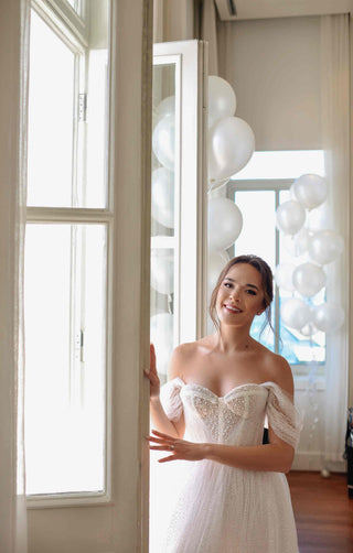 Chic wedding dress with a sparkling tulle skirt, beaded corset bodice, and romantic off-shoulder design, complemented by a dramatic veil