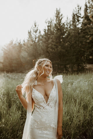 Minimalist lace bridal gown with a deep V-neckline, sheer floral detailing, and a fitted silhouette with a flowing train, designed for timeless and elegant weddings