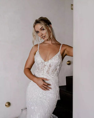 Elegant ivory wedding dress featuring intricate floral embroidery, deep V-neckline, thin straps, sexy backless style, and mermaid fit-and-flare design, ideal for romantic bridal looks