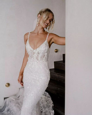 Custom ivory mermaid bridal gown with 3D floral lace applique and embroidery, V-neckline, thin spaghetti straps, backless design, and fit-and-flare silhouette, perfect for modern weddings