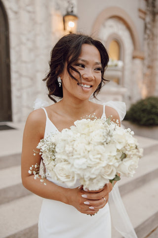 A timeless bridal look featuring a sleek white gown with delicate spaghetti straps and soft floral accents