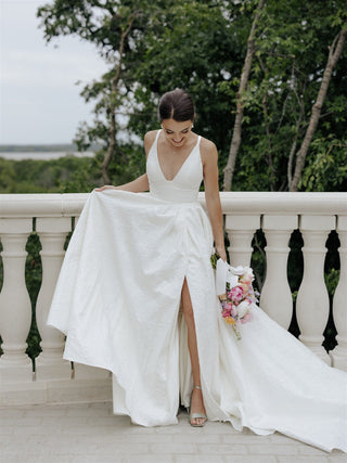 Romantic ivory gown adorned with textured fabric, a deep V-neckline, and a floor-length A-line silhouette, perfect for modern weddings and elegant bridal looks,