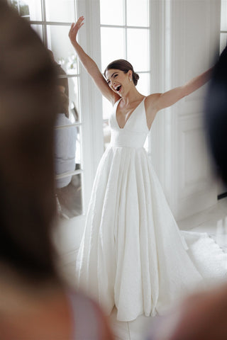 Ivory A-line wedding gown with a plunging V-neckline, textured fabric, and a flowing floor-length skirt, perfect for modern and elegant bridal celebrations