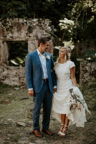 Simple ivory high-low wedding dress with cap sleeves, a fitted waist, and a flowing asymmetrical hem, perfect for relaxed outdoor ceremonies and rustic bridal styles