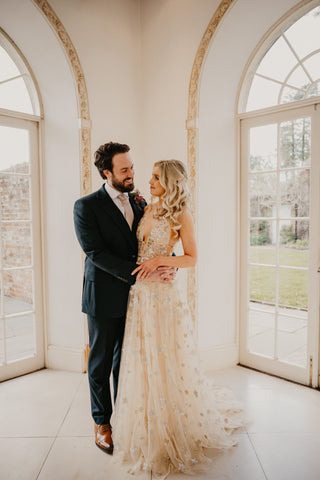 Cream beige ball gown with sparkly celestial starry sequin design, deep V-plunge neckline, and floor-length A-line silhouette, perfect as a unique bridal gown or prom dress for glamorous occasions