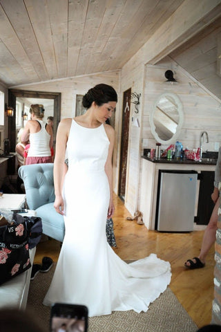 Minimalist ivory wedding gown with a high bateau neckline, sleeveless design, and a sleek floor-length silhouette with a flowing train, perfect for modern and elegant bridal styles