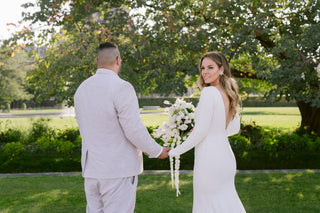 A refined and elegant choice for a modern bride, this gown showcases a seamless blend of structure and sensuality. The form-fitting silhouette is enhanced with exquisite floral lace on the sides, offering a glimpse of skin without compromising on sophistication. The long sleeves provide an elegant touch, while the side lacework creates a sense of drama and allure. This dress is ideal for brides looking for a balance between traditional bridal elegance and contemporary design.