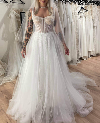 Chic ivory wedding dress with polka dot tulle layers, a fitted corset bodice, thin straps, and a flowing A-line skirt, paired with a sheer veil for a bohemian bridal style