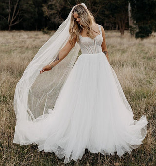 Ivory A-line wedding dress with a corset bodice, delicate polka dot tulle, and thin straps, styled with a flowing sheer veil, perfect for boho-inspired outdoor bridal celebrations