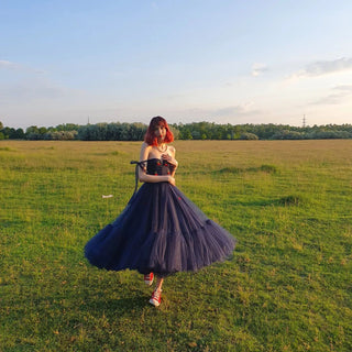 Elegant navy blue dress featuring a corset-style bodice adorned with red cherry accents, layered tulle skirt, and countryside backdrop