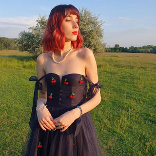 Whimsical navy tulle dress with cherry appliqués, delicate pearl necklace, and a serene outdoor setting at sunset