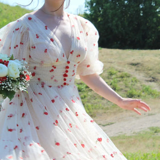 Ivory tulle midi dress with playful red cherry embroidery, a deep V-neckline, and sheer puff sleeves, perfect for whimsical garden parties and summer celebrations,