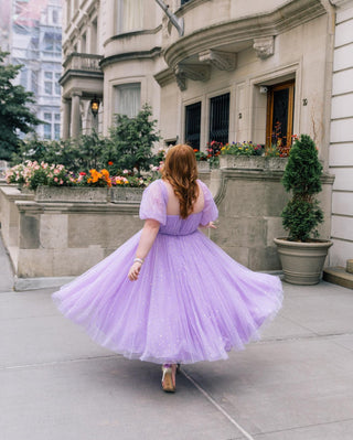 Whimsical lavender tulle dress with delicate glitter accents, flowing layers, and puff sleeves, creating a fairytale-inspired look.