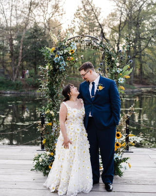 Ivory A-line ball gown with intricate yellow daisy embroidery, sheer tulle layers, and a sleeveless design, perfect for whimsical garden weddings and outdoor celebrations