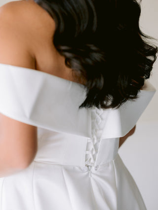 Chic and understated bridal gown showcasing an off-the-shoulder design, tailored bodice, and full skirt, perfect for both grand and intimate ceremonies