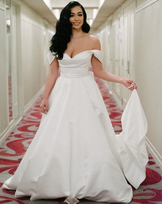 Modern and classic satin ball gown featuring an off-the-shoulder neckline, fitted bodice, and a voluminous skirt, ideal for elegant weddings