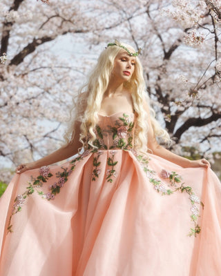 Peach tulle ball gown with intricate pink floral embroidery, strapless sweetheart neckline, and a flowing A-line silhouette, perfect for whimsical fairycore-inspired weddings or spring celebrations