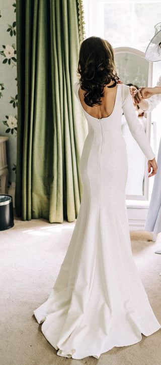 Romantic ivory gown with a square neckline, fitted long sleeves, and a flowing lace-embellished train, tailored for elegant and traditional bridal aesthetics