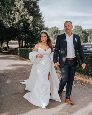 Elegant strapless wedding gown with a subtle sweetheart neckline, wrap detail, and a daring slit, perfect for a confident and stylish bride.

