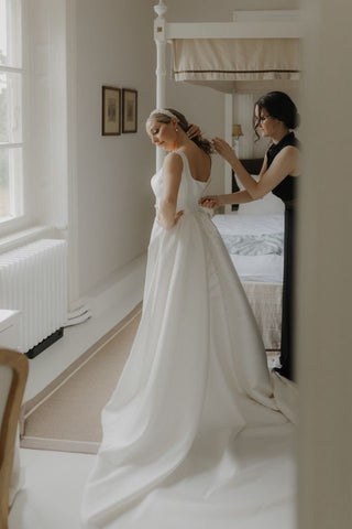 Elegant white bridal gown featuring a strapless bodice, pleated satin detailing, and a thigh-high slit, ideal for a chic and sophisticated wedding, complemented by soft curls and a bouquet of blush-toned flowers