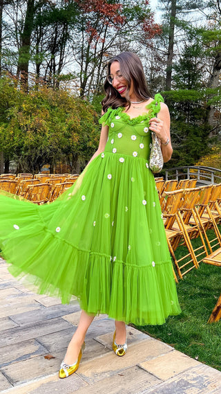 Vibrant green tulle dress adorned with dainty white daisy appliqués, featuring a ruffled neckline, fitted bodice, and flowy midi-length skirt, perfect for garden parties or spring celebrations