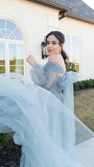 The gown is beautifully crafted with a fitted bodice, offering structure and shape, while the voluminous skirt flows gracefully to the floor. The soft blue hue, paired with the intricate, translucent layers of tulle, exudes a dreamy, fairy-tale vibe. The cinched waist accentuates the figure, making this gown a flattering choice for brides or anyone looking to stand out at a special event.