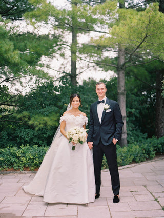 Graceful off-the-shoulder wedding gown featuring floral appliqués on the neckline, a structured bodice, and a voluminous A-line skirt.