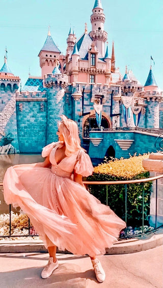 Whimsical blush pink tulle dress adorned with shimmering sequins, featuring a plunging neckline, puff sleeves, and a flowing midi-length skirt, styled with sneakers for a playful and magical look, perfect for Disney-themed outings or fairytale-inspired events