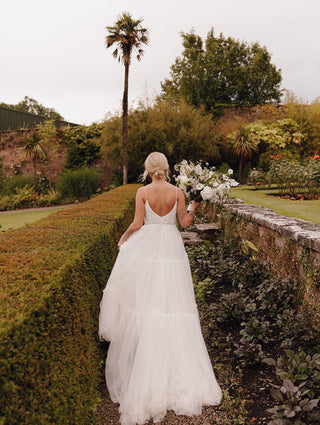 Timeless wedding dress with a cascading tulle skirt, fitted bodice with a deep V-neckline, and minimalist straps, perfect for creating an ethereal look for any wedding setting