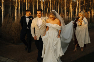 Luxurious white bridal dress featuring an off-the-shoulder neckline, corset-style bodice, and sweeping cathedral-length train for formal ceremonies.