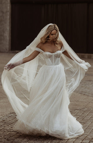 Ethereal off-shoulder wedding gown with a structured corset bodice, delicate beadwork, and flowing tulle skirt, styled with a sheer cathedral veil