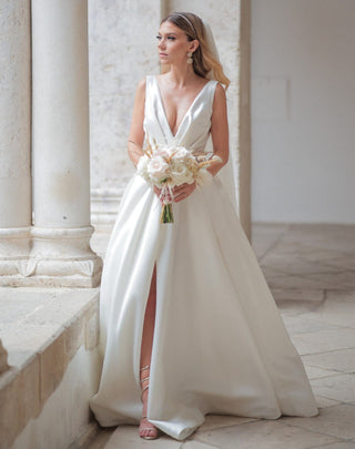 Elegant ivory bridal gown featuring a plunging neckline, sleek A-line silhouette, high slit, and satin fabric, ideal for sophisticated and romantic weddings