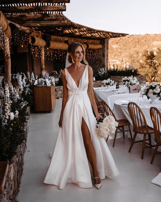 Ivory satin A-line wedding dress with a deep V-neckline, high leg slit, belted waist, and sleeveless design, perfect for modern outdoor bridal celebrations