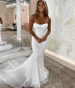 A sparkling white mermaid-style wedding gown with delicate spaghetti straps, perfect for a bride seeking glamour and sophistication