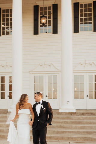 Elegant minimalist bridal gown with a strapless bodice and soft ruffle detail, flattering fitted design, styled with a natural greenery bouquet and warm-toned roses, ideal for modern weddings or intimate ceremonies