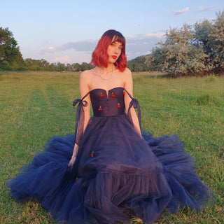 Romantic navy tulle gown with cherry embroidery, strapless bodice, and tied sheer straps, perfect for whimsical evening events