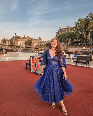 Cobalt dark blue ball gown with a gold sparkly starry celestial pattern, features a deep V-neckline, half puff sleeves, high leg slit, and midi tea-length design, perfect for formal occasions and glamorous evenings