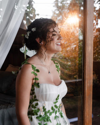 Elegant nature-inspired gown with soft tulle layers, green leaf motifs, and dainty flower details, suited for whimsical bridal aesthetics