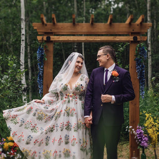 A stunning gown featuring a white tulle base adorned with vibrant floral embroidery in red, yellow, and green tones, creating a lively garden-inspired look