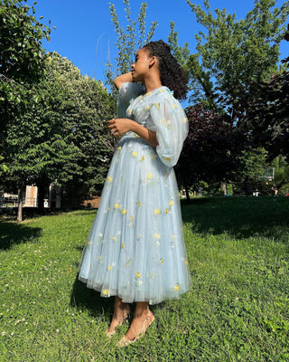 Light blue tea-length tulle dress with delicate yellow daisy embroidery, puff sleeves, and a flowy A-line silhouette, perfect for whimsical garden parties and outdoor celebrations