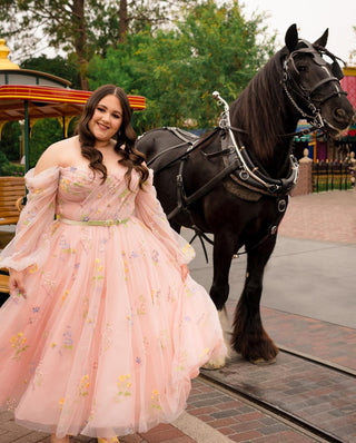 A pastel pink tulle gown adorned with delicate floral embroidery, creating a whimsical garden-inspired aesthetic