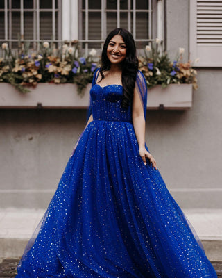 Cobalt dark blue ball gown with gold sparkly celestial starry design, features long cape sleeves and a sweetheart neckline, floor-length A-line glitter dress perfect for weddings, prom, and glamorous events