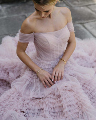 Romantic pink tulle dress with intricate tiered ruffle details, fitted bodice with off-the-shoulder straps, and a voluminous skirt, ideal for elegant evening wear or dreamy bridal looks