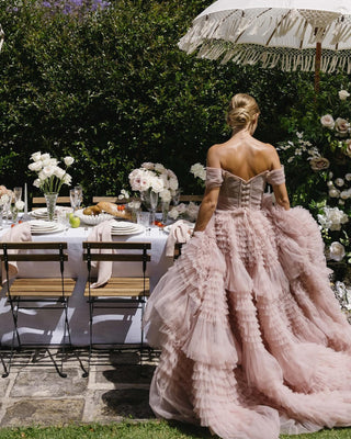 Romantic pink tulle dress with intricate tiered ruffle details, fitted bodice with off-the-shoulder straps, and a voluminous skirt, ideal for elegant evening wear or dreamy bridal looks