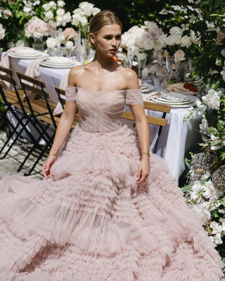 Chic blush tulle dress featuring cascading ruffle tiers, a fitted corset-style bodice, and elegant off-the-shoulder sleeves, perfect for grand entrances at weddings or gala events