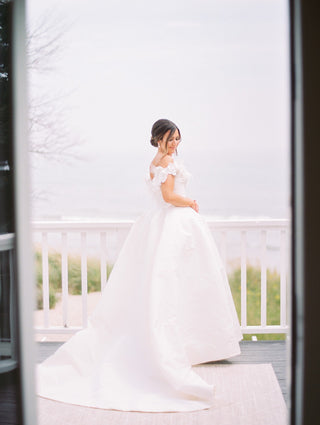 Sophisticated bridal attire adorned with floral appliqués, highlighting an off-the-shoulder neckline and a regal ball gown silhouette ideal for formal ceremonies